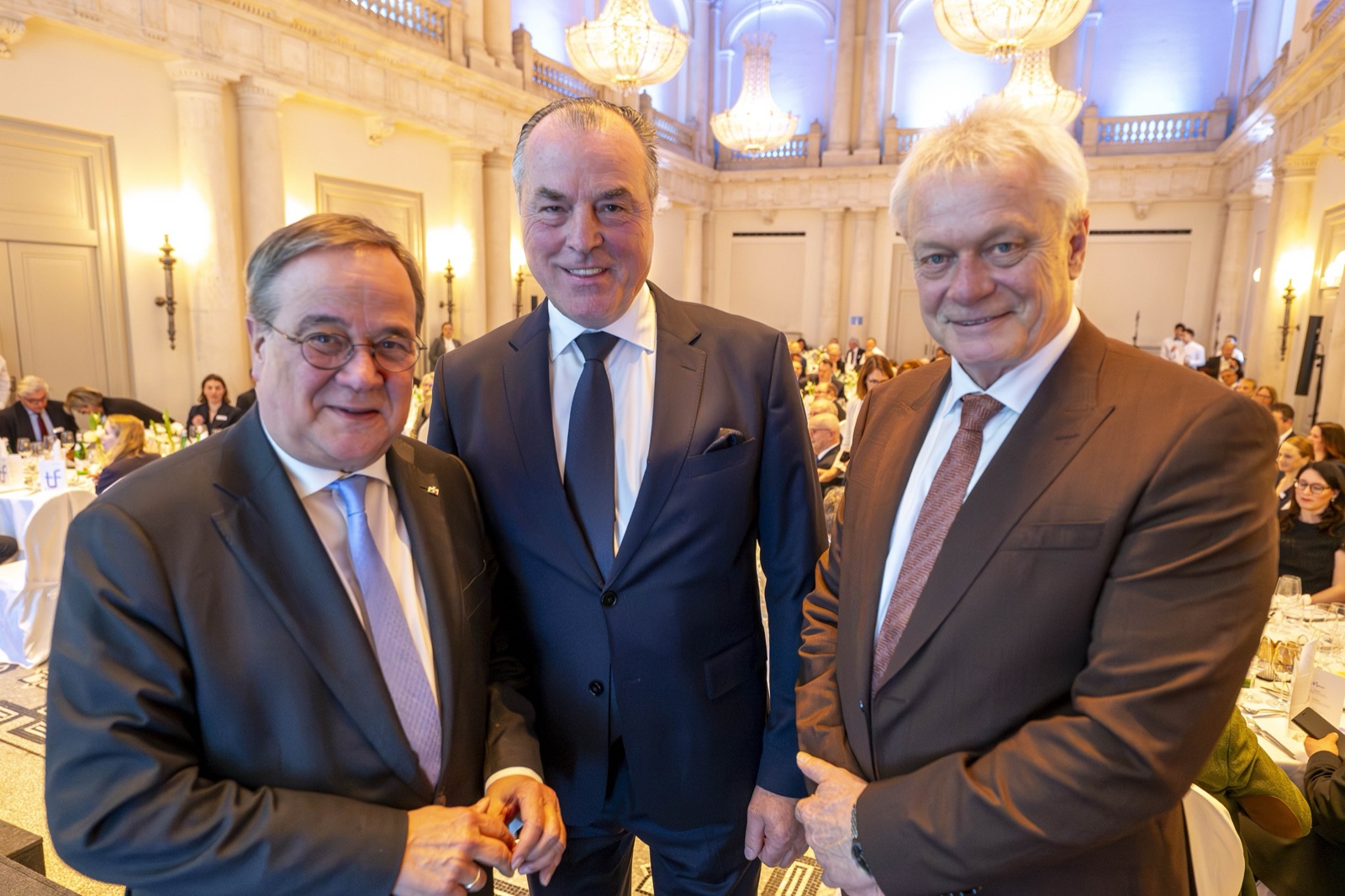 Three men in suits smiling at a formal event in a hall with chandeliers: Armin Laschet, Clemens Tönnies and Alois Rainer