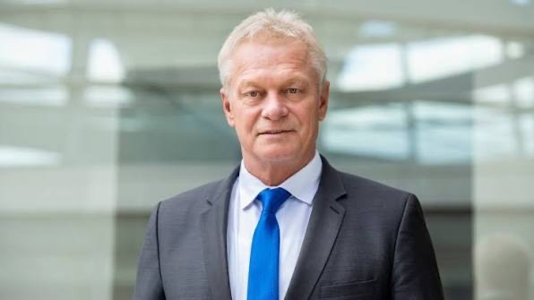 Alois Rainer in a grey suit and blue tie in front of a glass facade