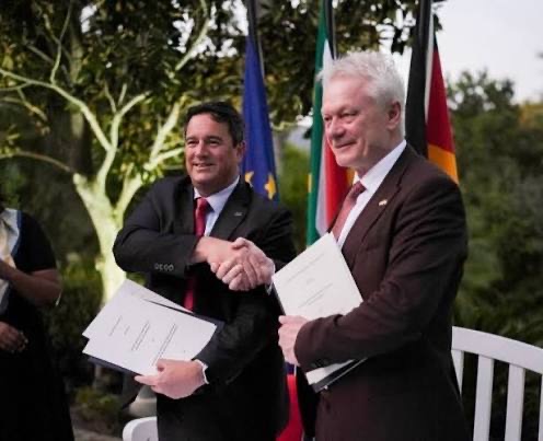 Two ministers shaking hands holding documents in front of flags