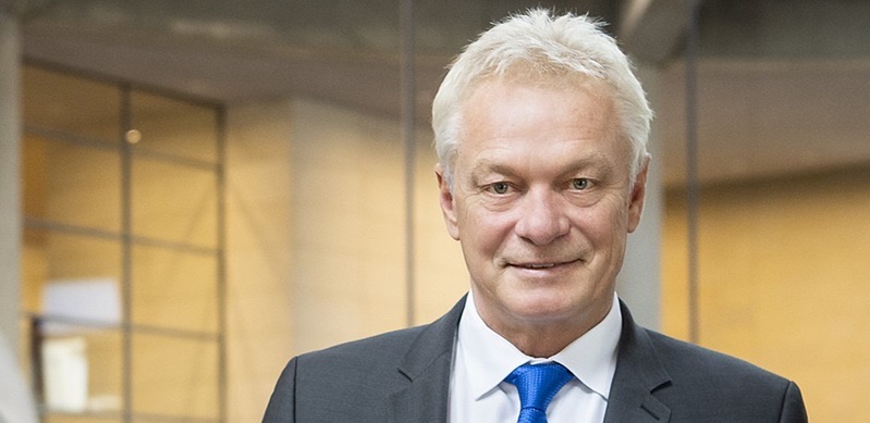 Alois Rainer smiling in a dark suit and blue tie in a bright Bundestag building