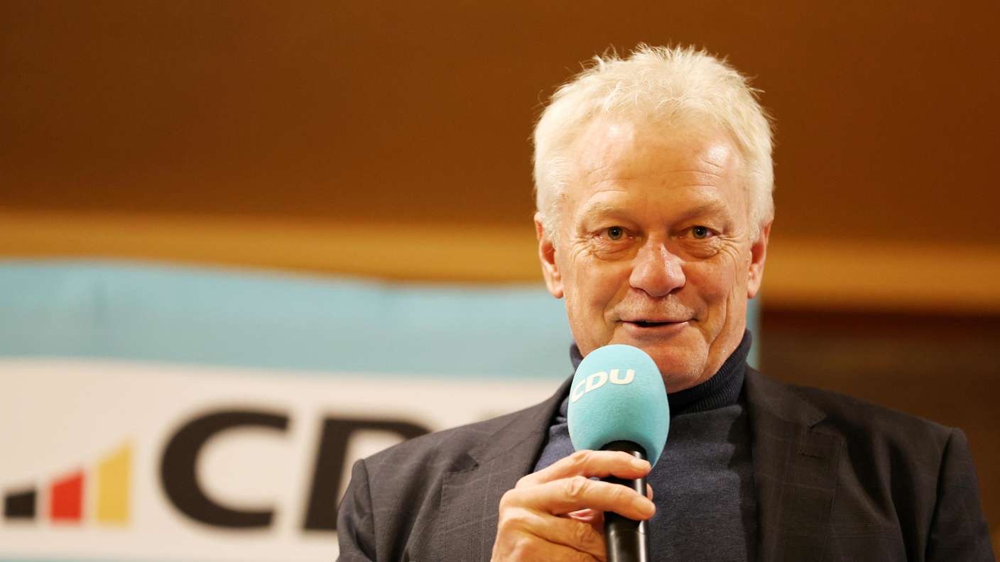 Alois Rainer speaking into a microphone at a party event, smiling
